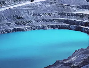 An open-pit mine with water, surrounded by terraced rock walls and mining equipment
