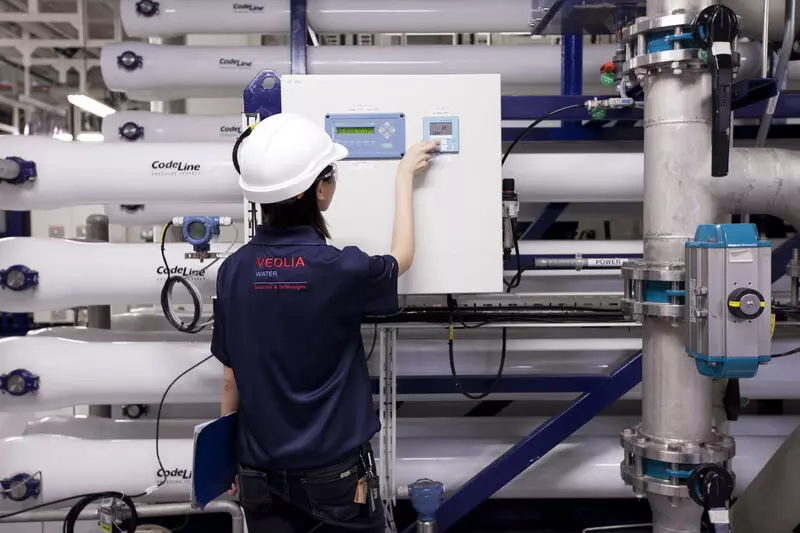 Veolia staff wearing a white safety helmet operating a control panel at a water and wastewater treatment system