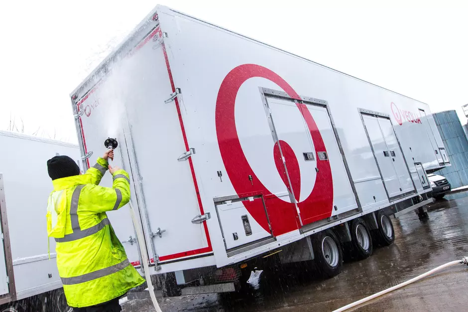 Veolia worker in a neon jacket washing a mobile water treatment unit trailer with a water hose